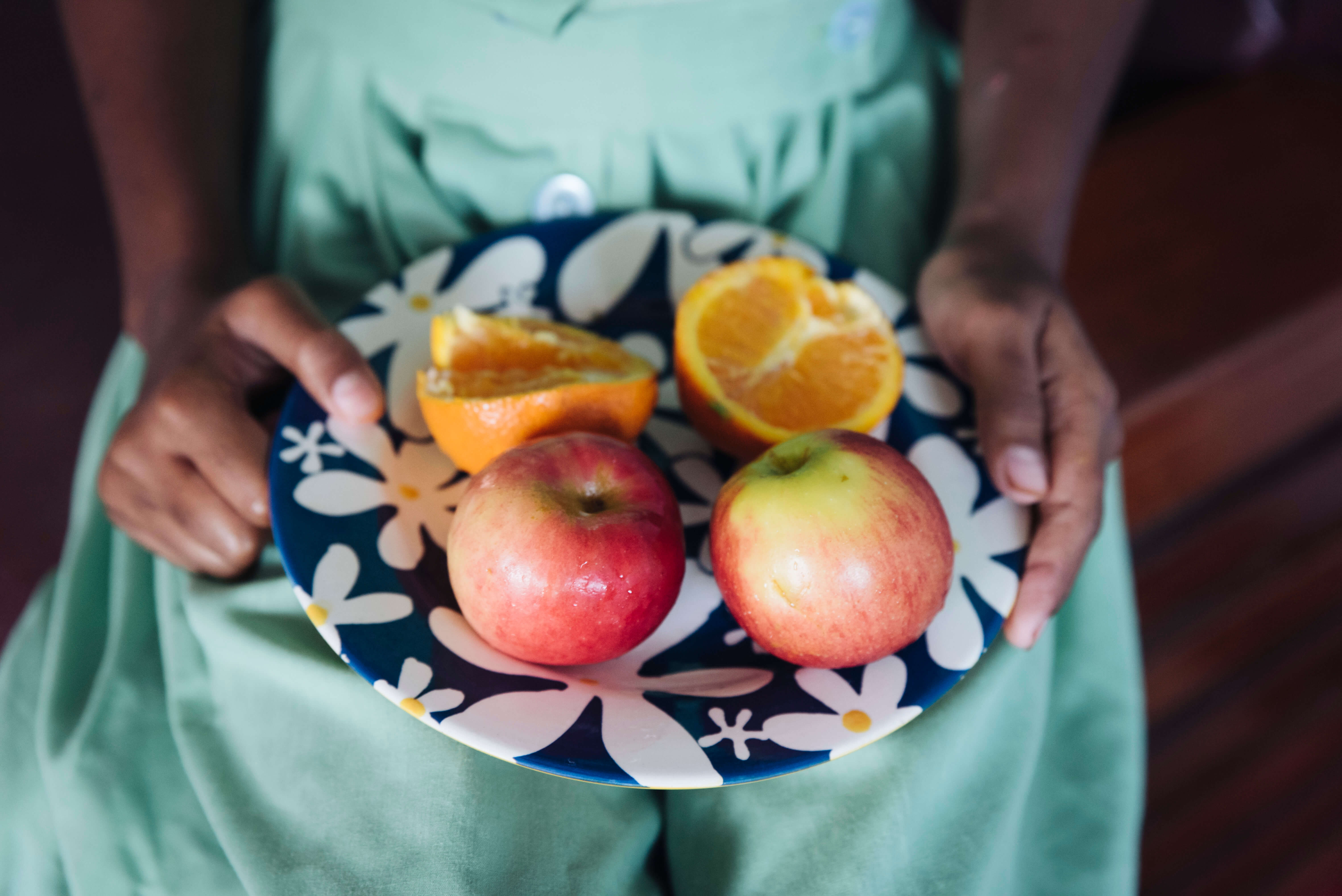 A Fijian school student holds a plate of apples and cut oranges.
