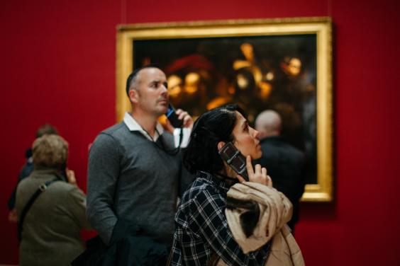 Man and woman hold dedicated audio tour device to their ears in an art gallery